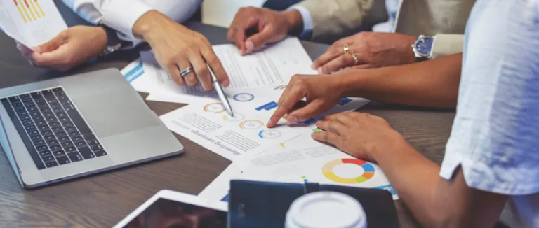 different peoples arms on a table with a computer and a bunch of papers business law
