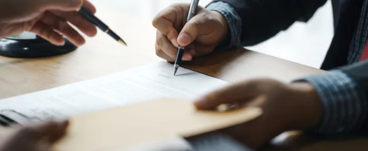 one person writing on a paper with a pen and another person holding a pen