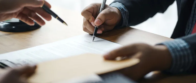 one person writing on a paper with a pen and another person holding a pen