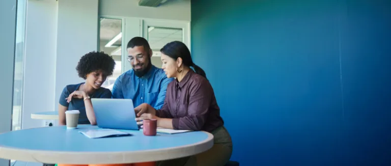 two women and a man sitting at a round table looking at a laptop general counsel