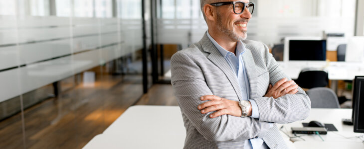 Successful authoritative confident mature grey-haired adult male entrepreneur businessman professional in formal wear standing at the modern home office, looking at camera